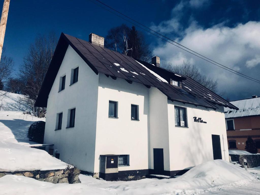 a white house with a black roof in the snow at Chata Hella in Pernink