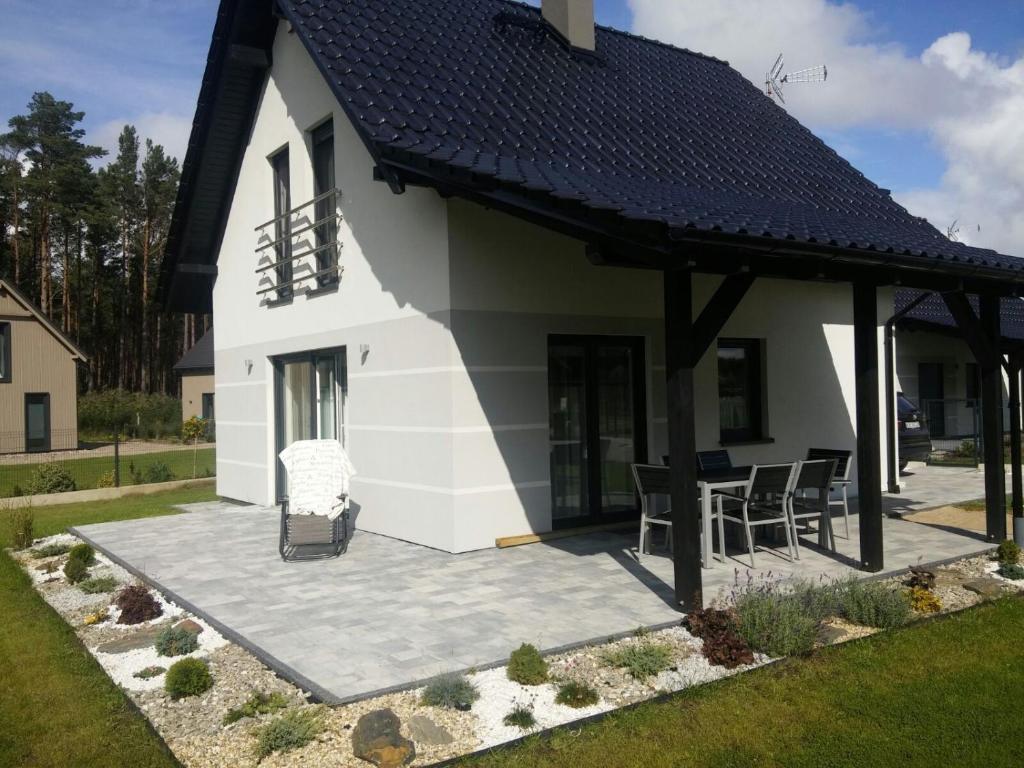 a white house with a black roof and a patio at Domek na Plażowej Lubiatowo in Lubiatowo