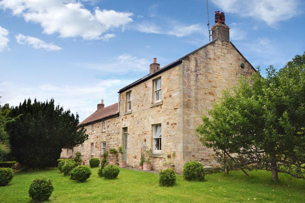 an old stone building with trees in front of it at Mill House Cottage in Morpeth