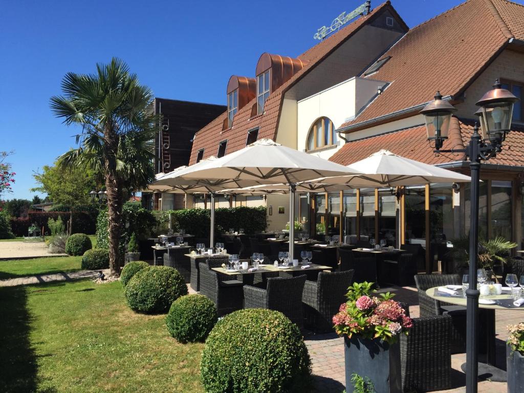 a restaurant with tables and umbrellas in front of a building at Hotel De Kommel in Voeren