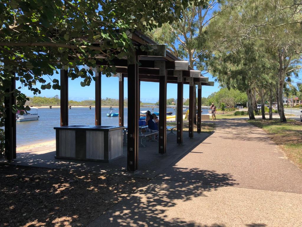 a park with people sitting on a bench next to the water at Bayz on the River in Maroochydore