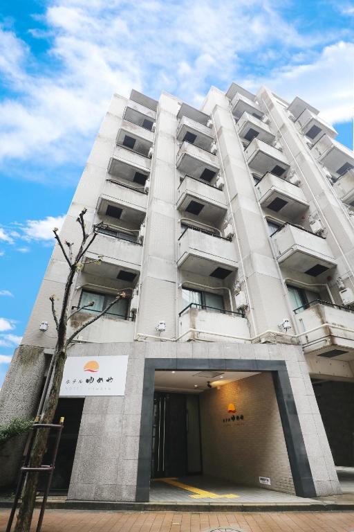 a tall white building with a tree in front of it at Hotel Yumeya in Fukuoka
