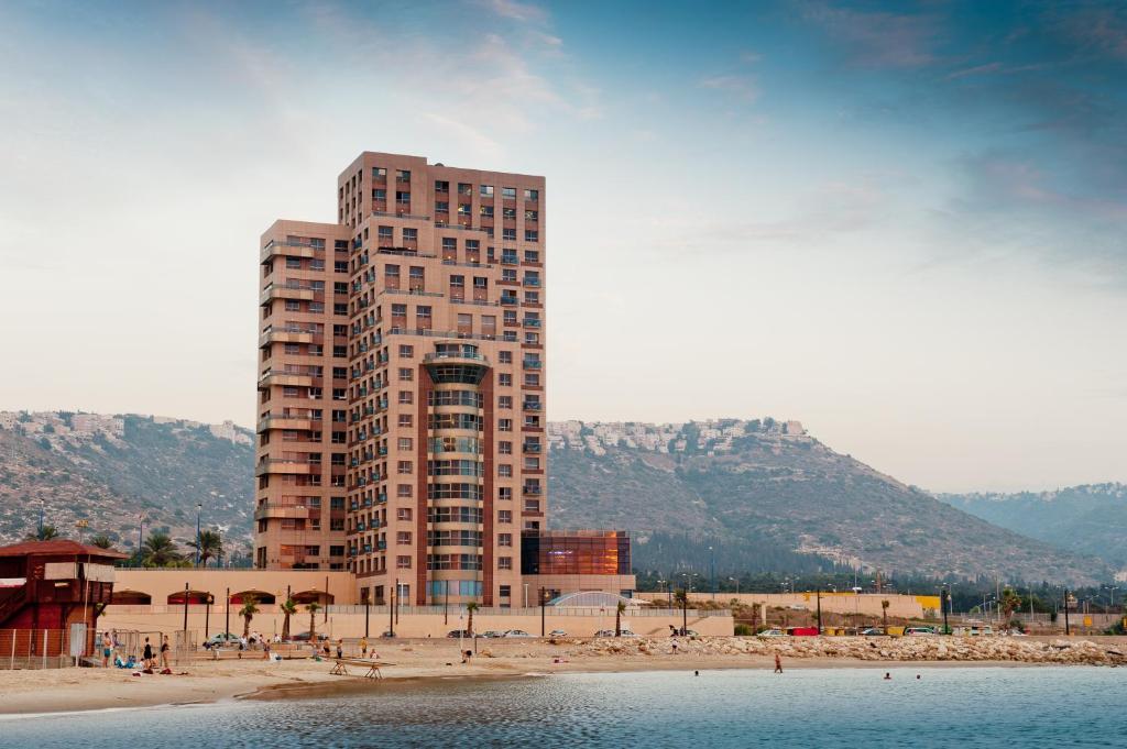 a tall building on a beach with a building at Leonardo Plaza Haifa in Haifa