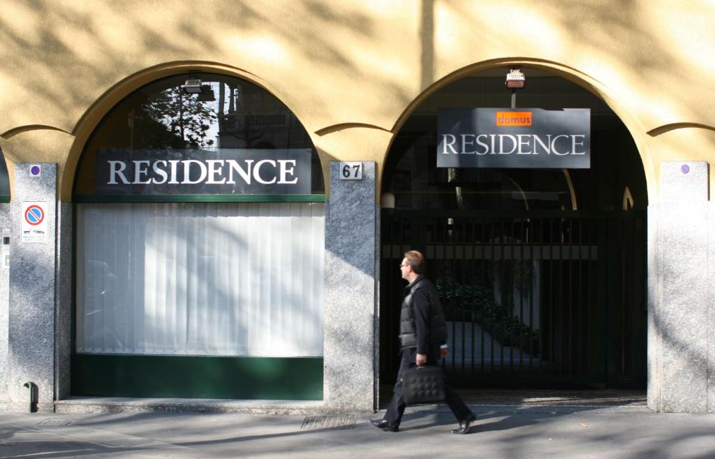 un hombre caminando delante de un edificio con un signo de referencia en Residence Domus, en Milán