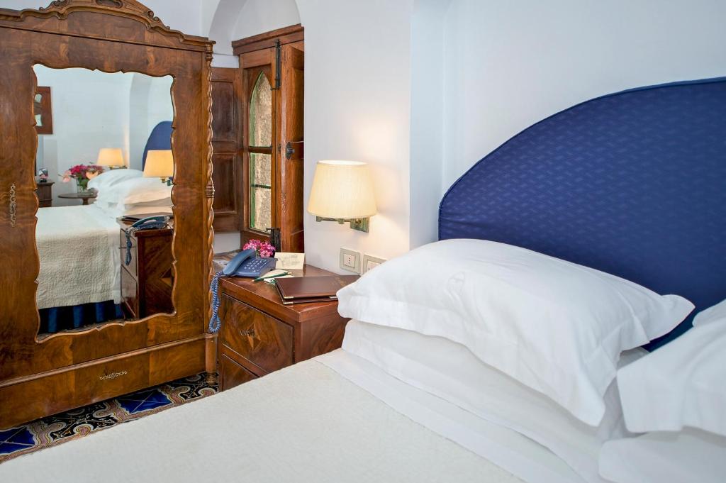 a bedroom with a bed with a blue headboard and a mirror at Hotel Villa Cimbrone in Ravello