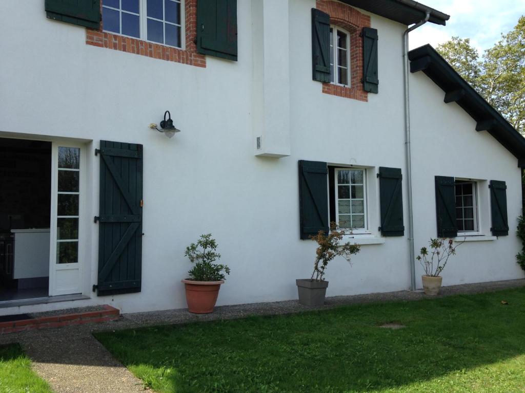 ein weißes Haus mit schwarzen Rollläden und einem Hof in der Unterkunft Meublé Maison Narbay in Saint-André-de-Seignanx