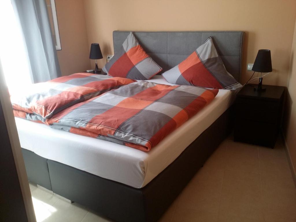 łóżko z pomarańczowymi i szarymi kocami i poduszkami w obiekcie Ferienwohnung Tropical w mieście La Herradura