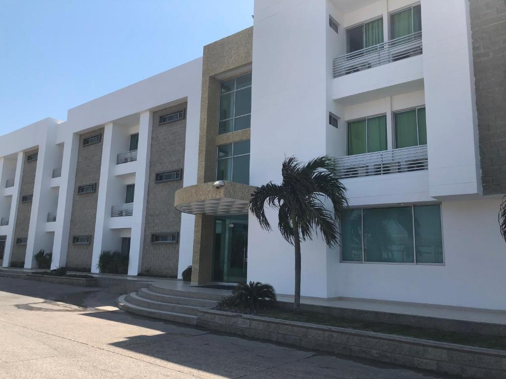 a white building with a palm tree in front of it at Hotel Via 40 in Barranquilla