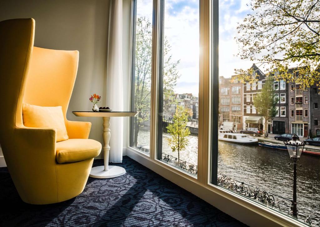 une chaise jaune assise devant une grande fenêtre dans l'établissement Andaz Amsterdam Prinsengracht - a concept by Hyatt, à Amsterdam