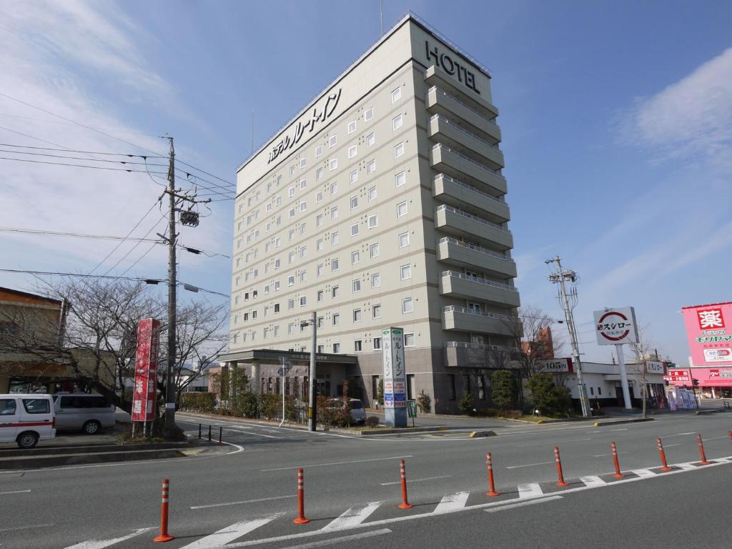 a tall white building on a city street at Hotel Route-Inn Matsusaka Ekihigashi in Matsuzaka