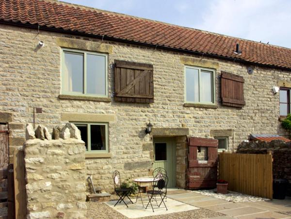 een stenen huis met een tafel en stoelen ervoor bij Cow Byre Cottage in Pickering