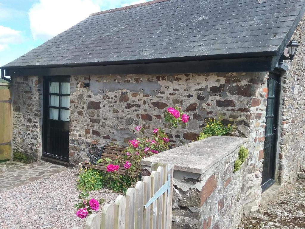 een stenen gebouw met een zwart dak en bloemen bij The Old Workshop in Knowstone