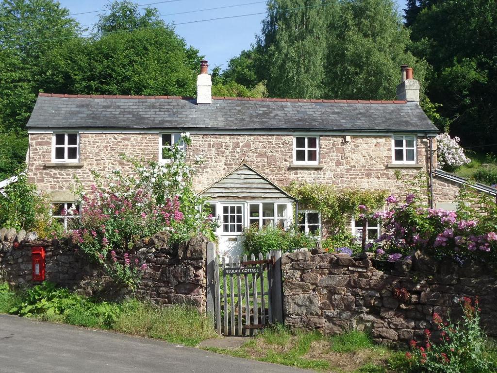 una casa de ladrillo con una valla de piedra y flores en Beulah Cottage en Cinderford