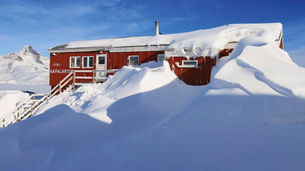 a red house covered in snow with a pile of snow at The Red House in Tasiilaq