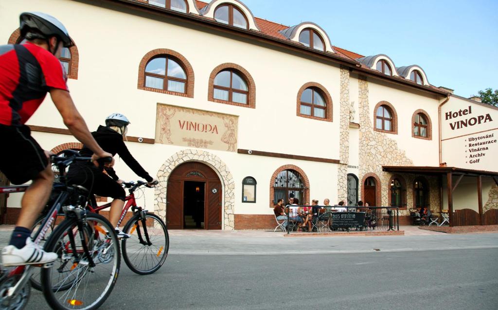 two people riding bikes in front of a building at Hotel Vinopa in Hustopeče