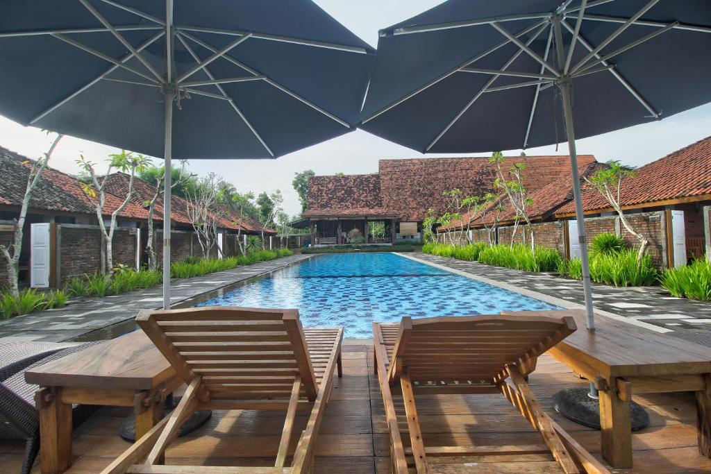 a swimming pool with two chairs and two umbrellas at Shankara Borobudur in Borobudur
