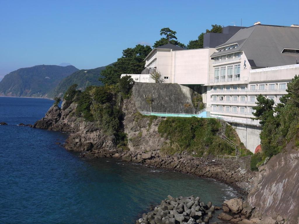 a building on a cliff next to the water at Itoen Hotel Toi in Izu