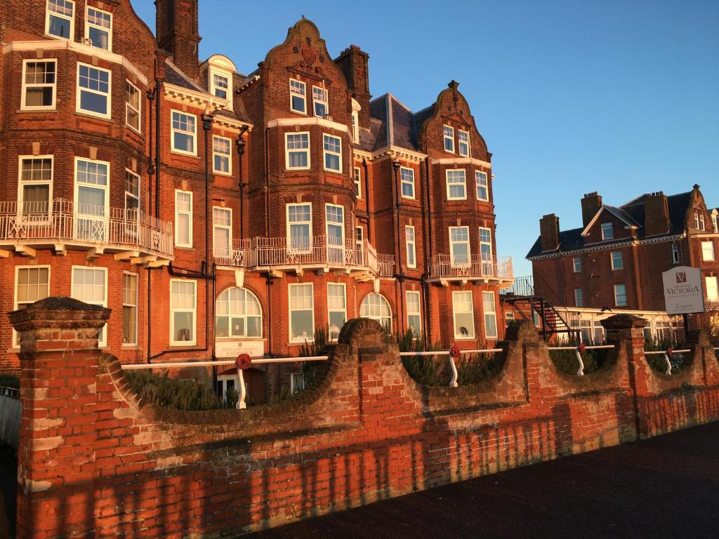 un grand bâtiment en briques rouges avec une clôture devant lui dans l'établissement Hotel Victoria, à Lowestoft