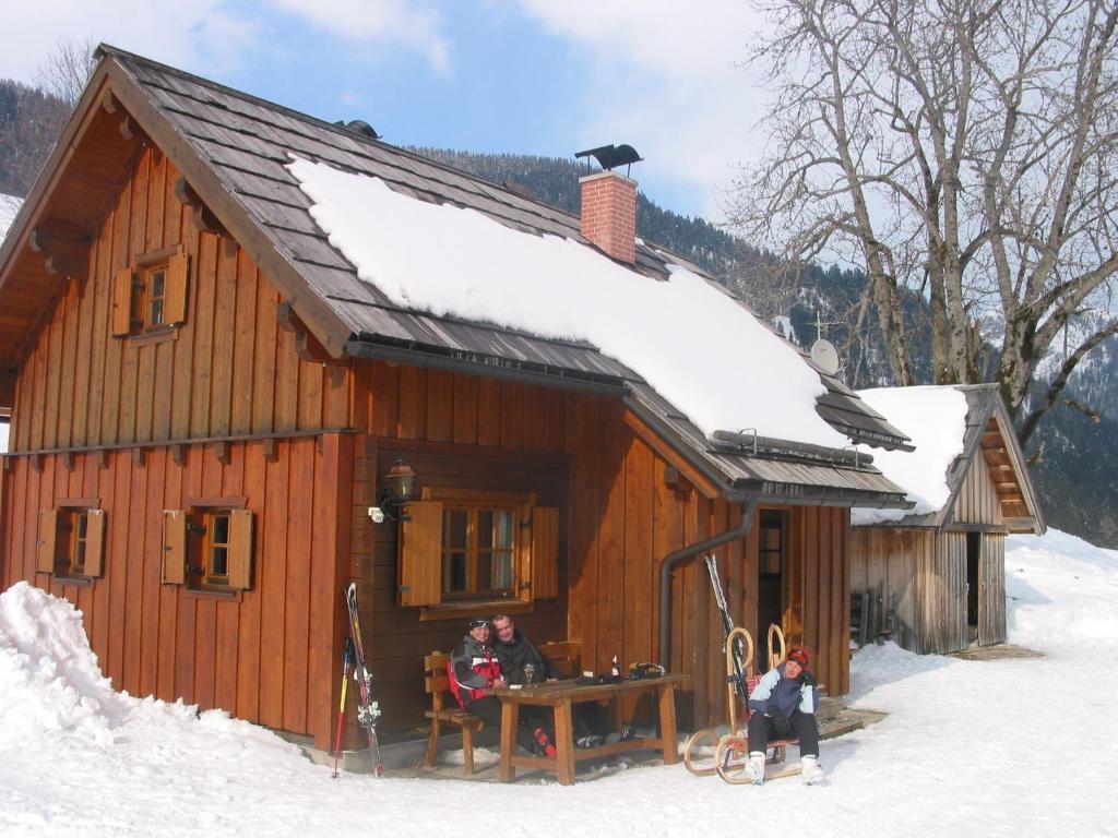 two people sitting outside of a cabin in the snow at Egghartguthütte in Tauplitz