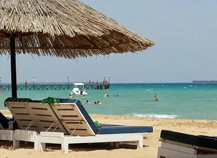 a beach with an umbrella and chairs and people in the water at Palmera El Sokhna Chalets Families Only in Ain Sokhna