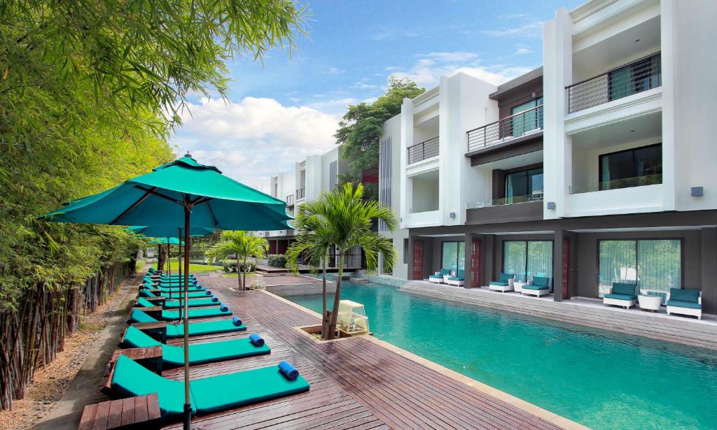 a row of lounge chairs with an umbrella next to a swimming pool at The Serenity Hua Hin in Hua Hin