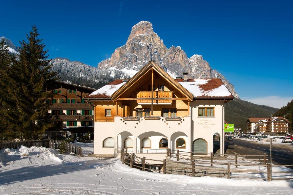 un edificio en la nieve con una montaña en el fondo en Appartamenti Villa Olympia, en Corvara in Badia