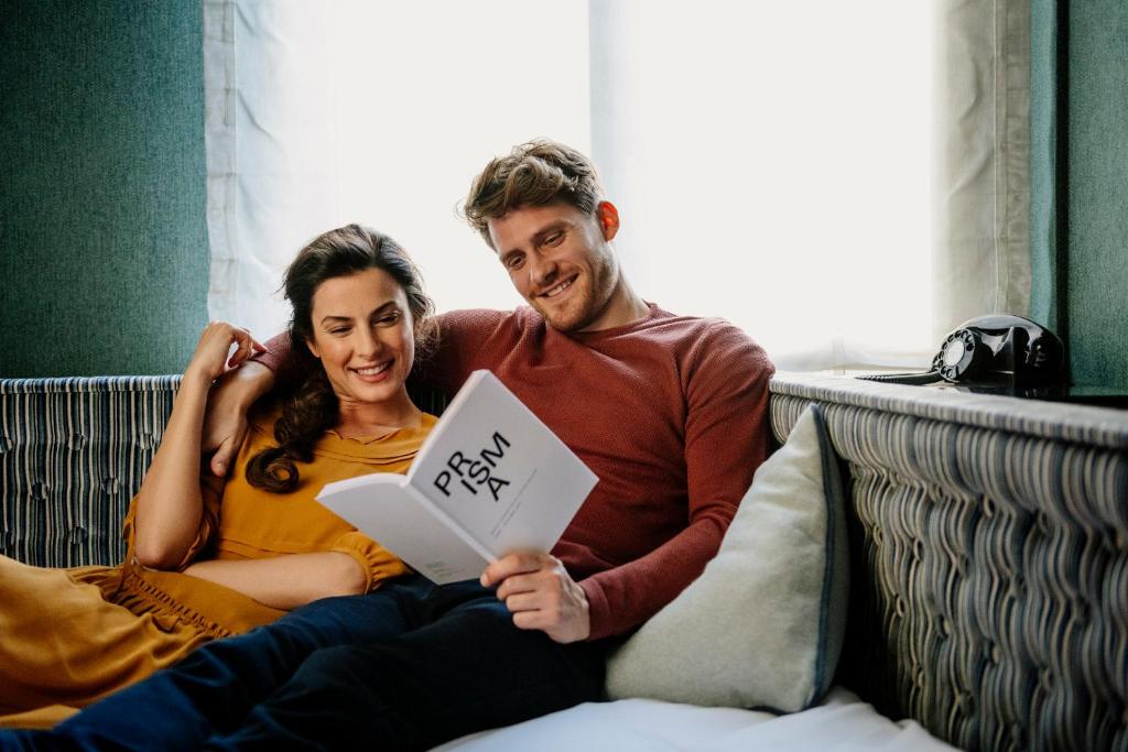 a man and woman sitting on a bed reading a book at Opera Hotel Zürich in Zürich
