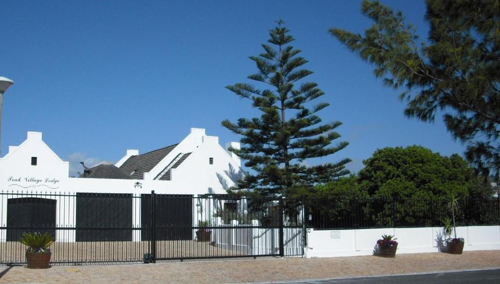 a tree in front of a white house with a fence at Peak Village Lodge in Bloubergstrand