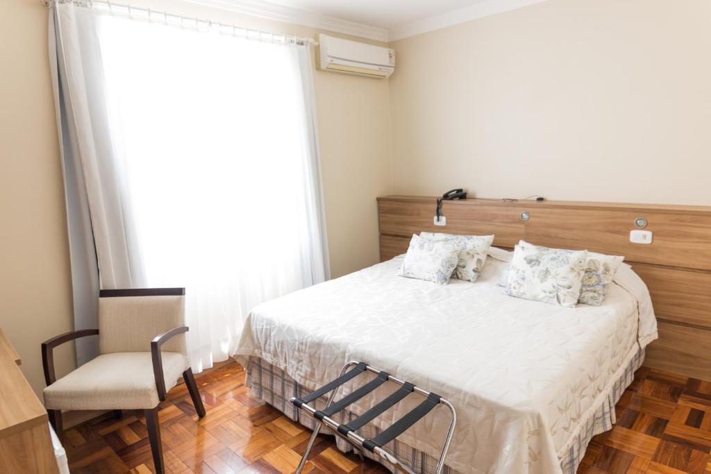 ein Schlafzimmer mit einem Bett, einem Stuhl und einem Fenster in der Unterkunft Hotel Princesa dos Vales in Veranópolis