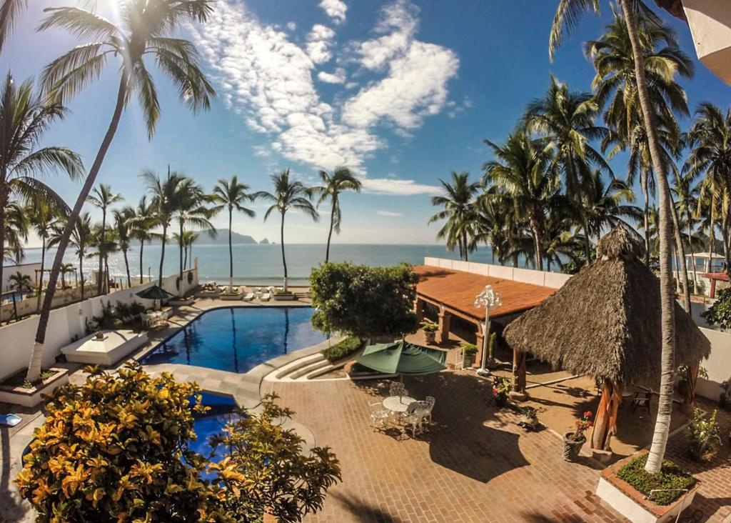 a resort pool with palm trees and the ocean at Hotel Posada Pablo de Tarso in San Patricio Melaque