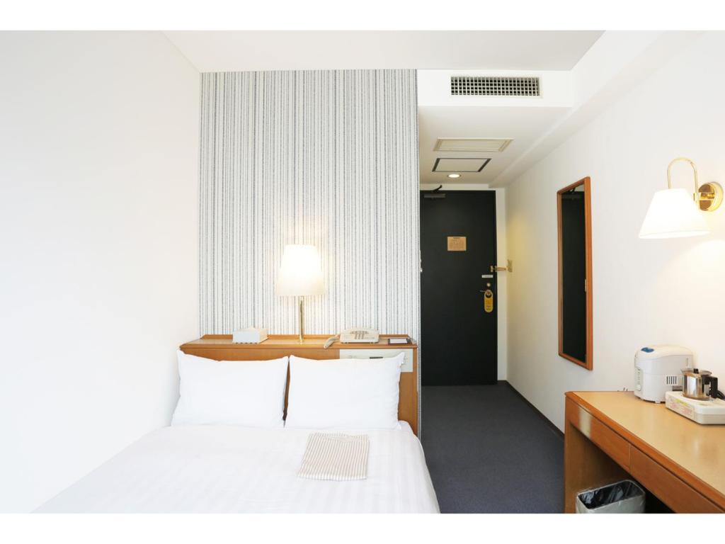 a hotel room with a bed and a desk with a lamp at Smile Hotel Nihombashi Mitsukoshimae in Tokyo