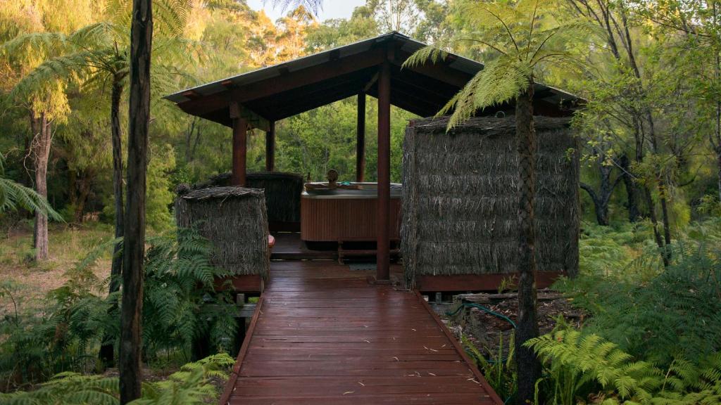 a wooden walkway leading to a hot tub in a forest at Mudstone Spa Retreat in Pemberton