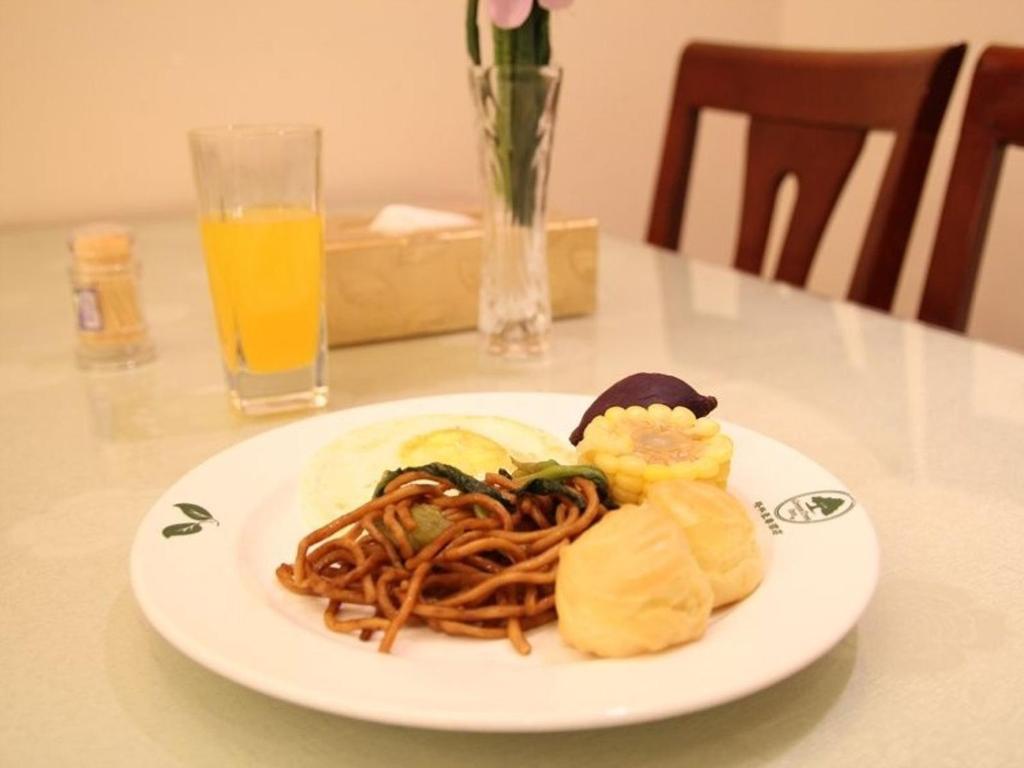 a plate of spaghetti on a table with a glass of orange juice at GreenTree Inn Anhui HeFei West Changjiang Road Fengle Building Express Hotel in Hefei