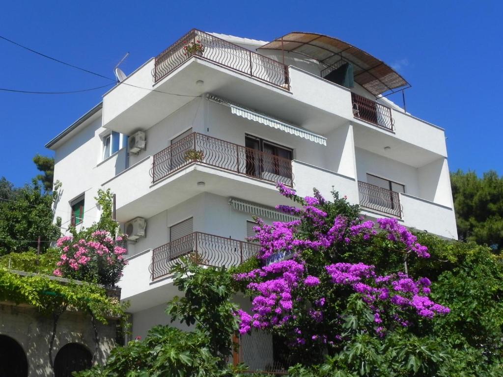 a white building with purple flowers in front of it at Apartments STANIĆ - apartments with a view of the sea and sandy beach in Duće