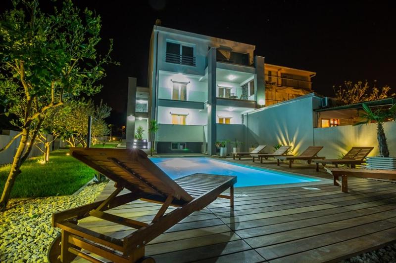 a house with a swimming pool in front of a building at Apartmani Pocco Locco in Biograd na Moru