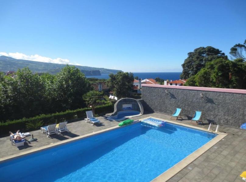 a swimming pool with chairs and the ocean in the background at Quinta Nossa Senhora de Lourdes in Capelas