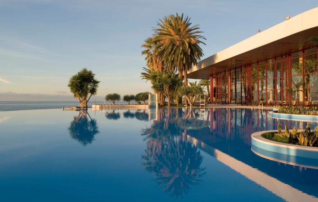 une piscine avec un bâtiment et des palmiers dans l'établissement Pestana Casino Park Hotel & Casino, à Funchal