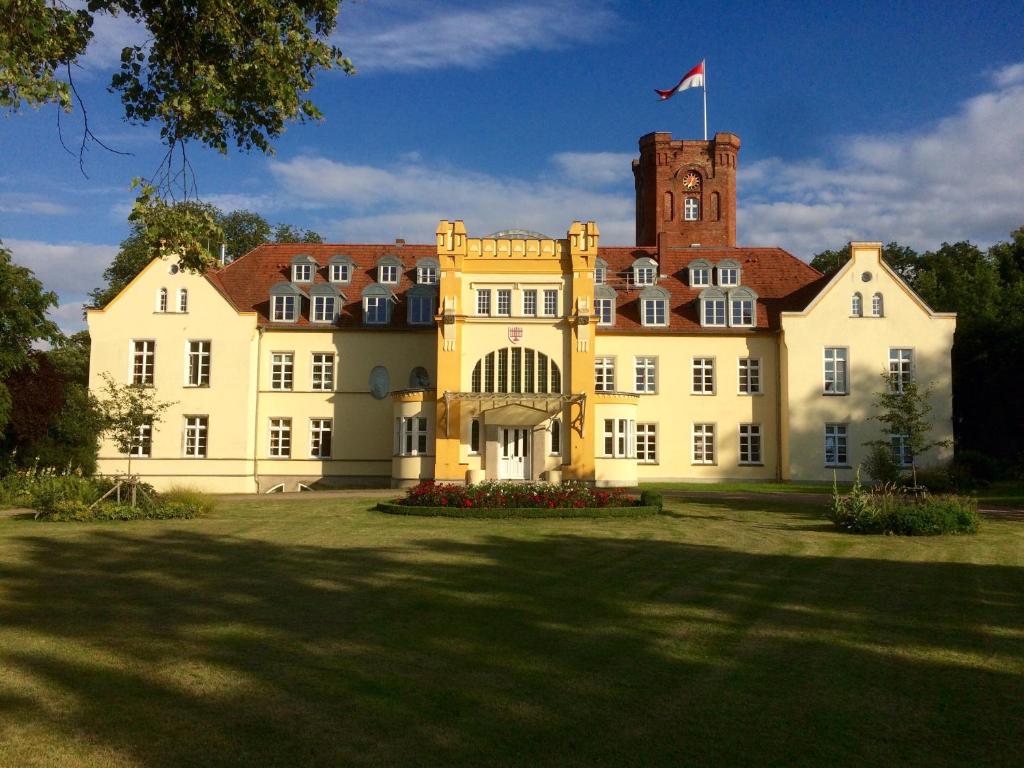 ein großes gelbes Gebäude mit einer Flagge darüber in der Unterkunft Schloss Lelkendorf - Fewo Prebberede in Lelkendorf
