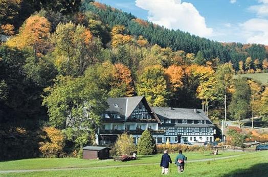 dwoje ludzi idzie przed dużym domem w obiekcie Tommes Gästehaus Zur Mühle w mieście Schmallenberg