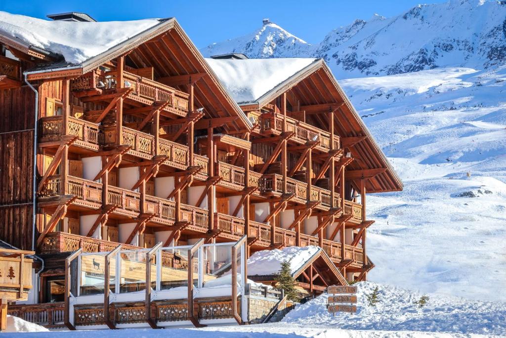 a large wooden building in the snow with mountains at Hôtel Au Chamois d'Or by Les Etincelles in L'Alpe-d'Huez