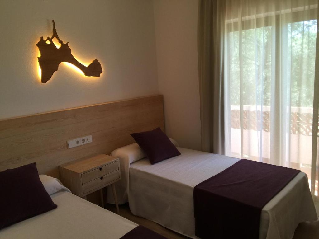 a bedroom with two beds and a window and a lamp at Apartamentos DELFIN in Es Calo