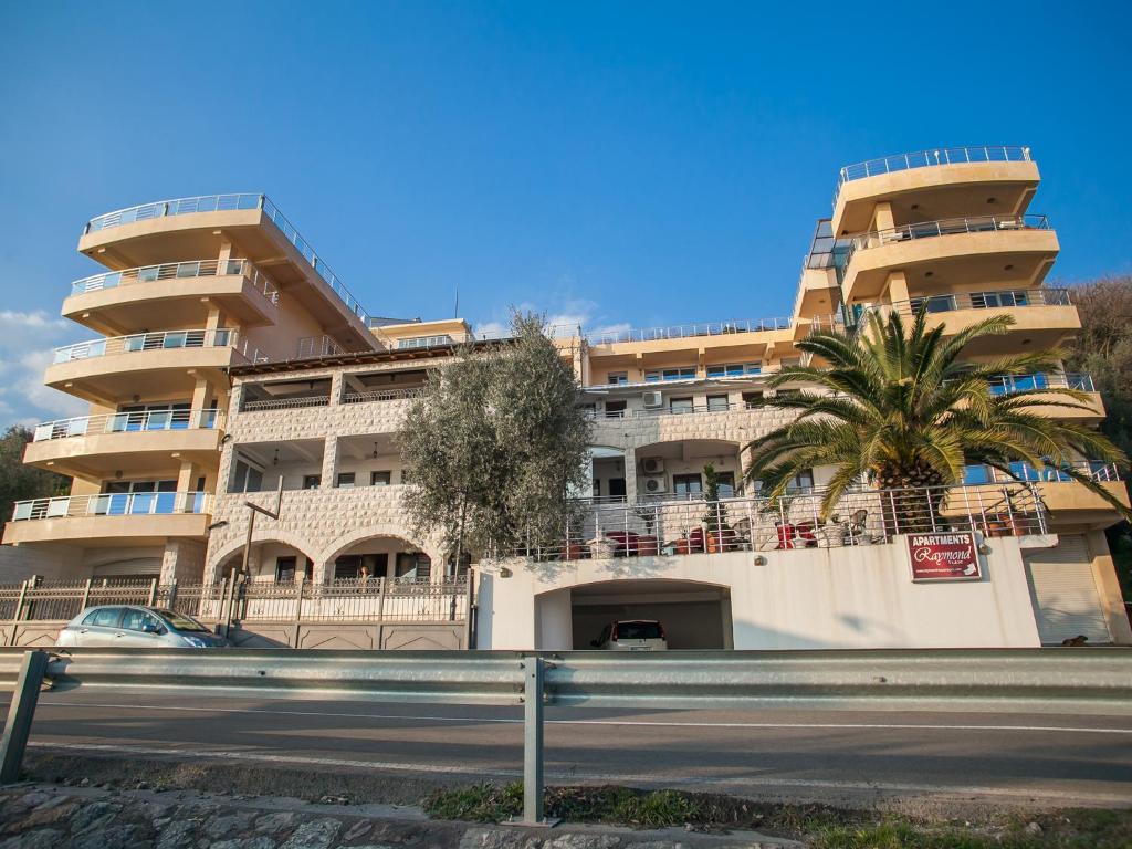 a building with a palm tree in front of a street at Apartments Raymond in Sveti Stefan