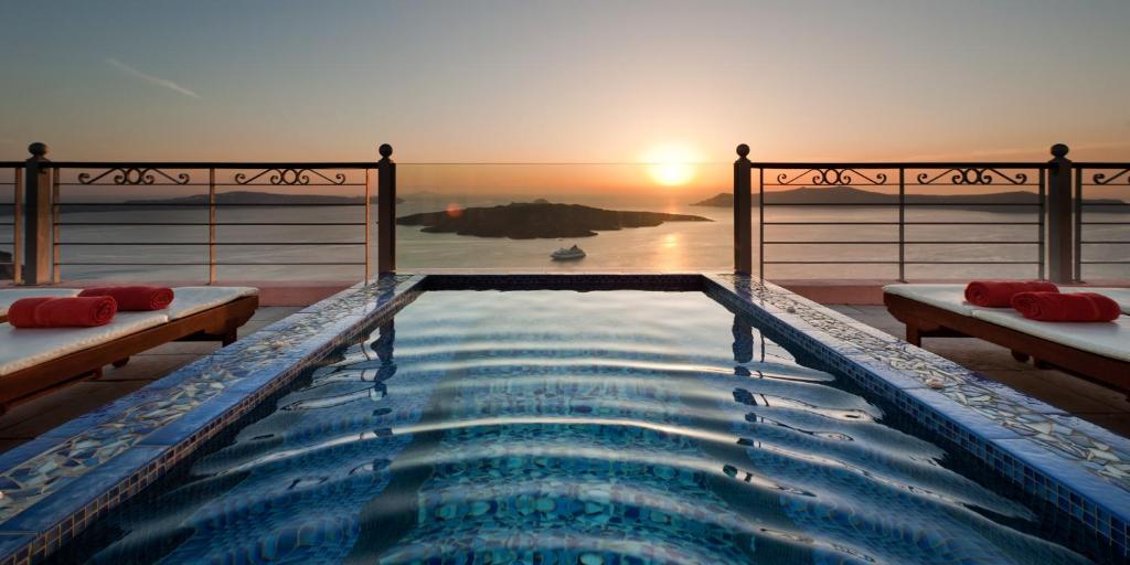 una piscina con puesta de sol en el fondo en Nefeles Luxury Suites, en Fira