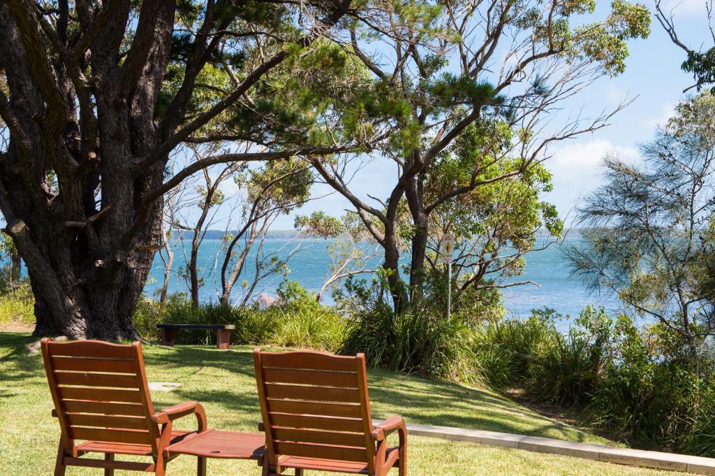 due sedie sedute sull'erba vicino all'acqua di By the Beach B&B Self Contained Apartments a Sanctuary Point