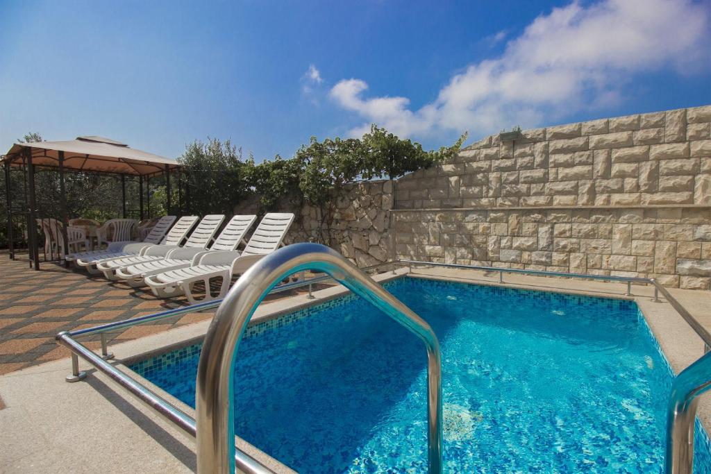 a swimming pool with chairs next to a stone wall at Apartments Lenija in Jadrija