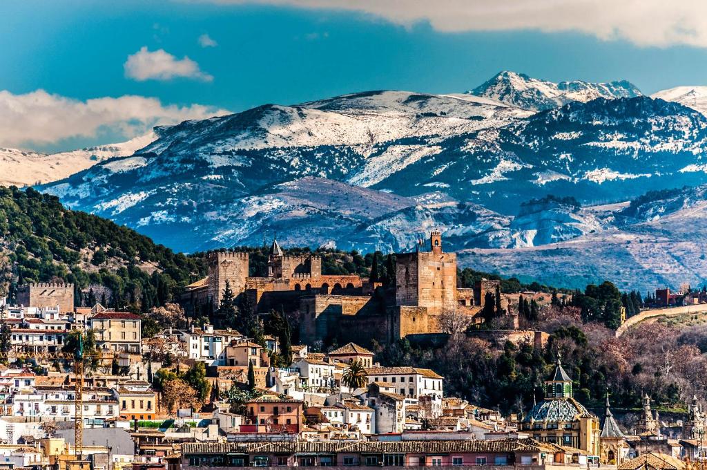 a city with a castle on a hill with snow covered mountains at Residencial el Molino Churriana in Churriana de la Vega