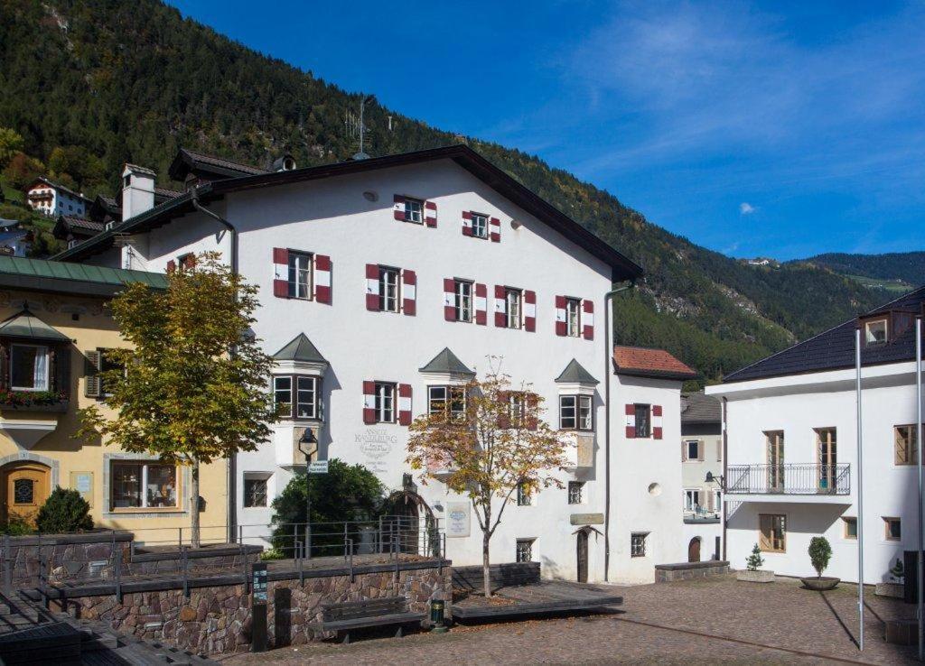 ein großes weißes Gebäude mit roten Fenstern und einem Berg in der Unterkunft Hotel Ansitz Kandelburg in Mühlbach