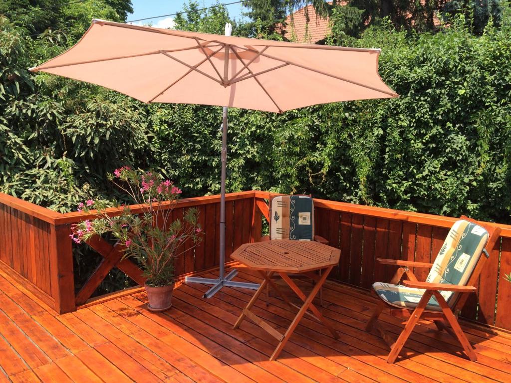 eine Holzterrasse mit einem Tisch, Stühlen und einem Sonnenschirm in der Unterkunft Anonim apartman in Villány