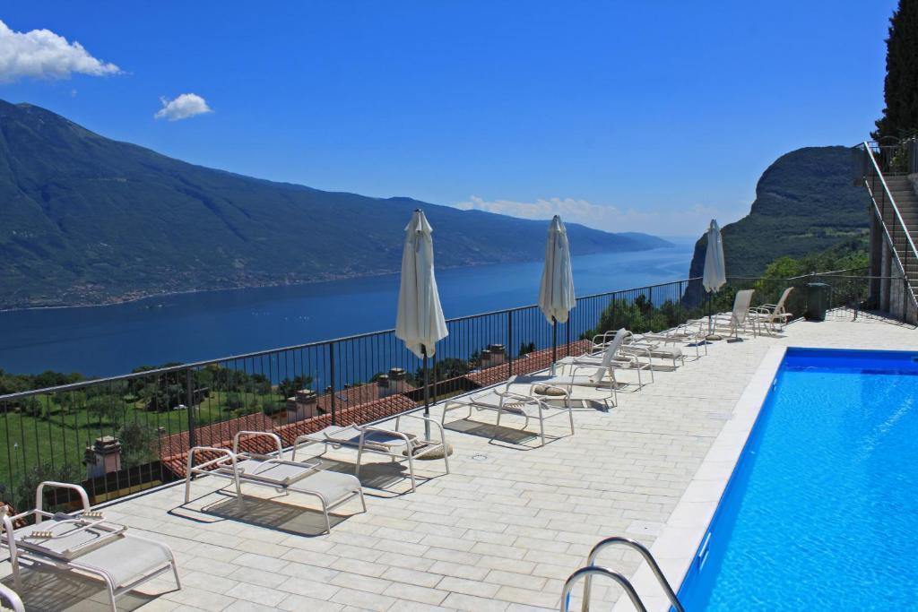 einen Pool mit Stühlen und Sonnenschirmen neben dem Wasser in der Unterkunft La Quiete 56 Lake view Apartment by Gardadomusmea in Tremosine sul Garda