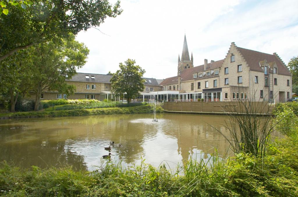a pond in front of a building with a church at Hotel Oude Abdij in Lo-Reninge